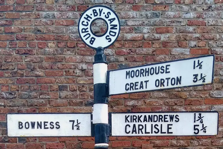 A cast-iron Cumberland County Council fingerpost near Carlisle, its arms pointing to Carlisle, Bowness, Kirkandrews, Moorhouse and Great Orton