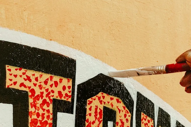 A sign painter's hand and brush, mid-stroke, lettering a name onto a wall